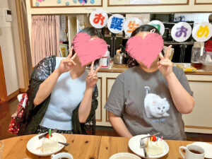 ケーキを前に座った2人が、笑顔でピースをしている写真。後ろには「お誕生日おめでとう」の飾りがかかっている。