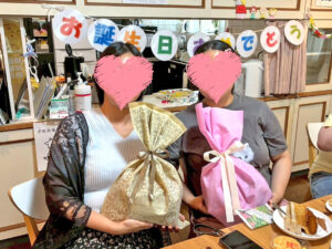 プレゼントを抱えた2人が並んで座っている写真。背景には「お誕生日おめでとう」の文字飾りが見える。